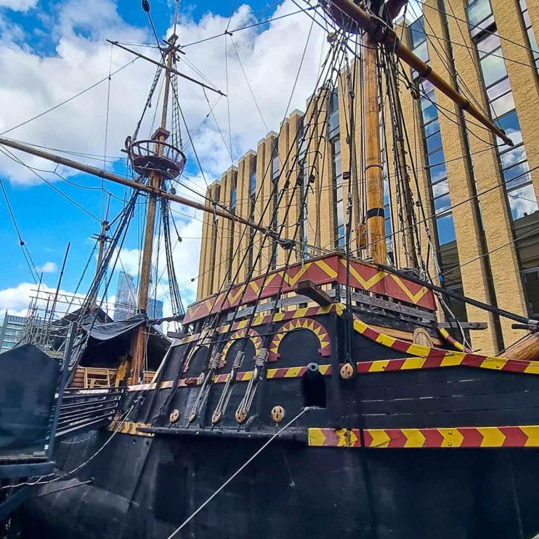 Side view of the Golden Hinde replica Tudor galleon in Southwark, one mast seen against a blue sky and buildings behind - my Escape from the Golden Hinde review of a new escape room in London with kids