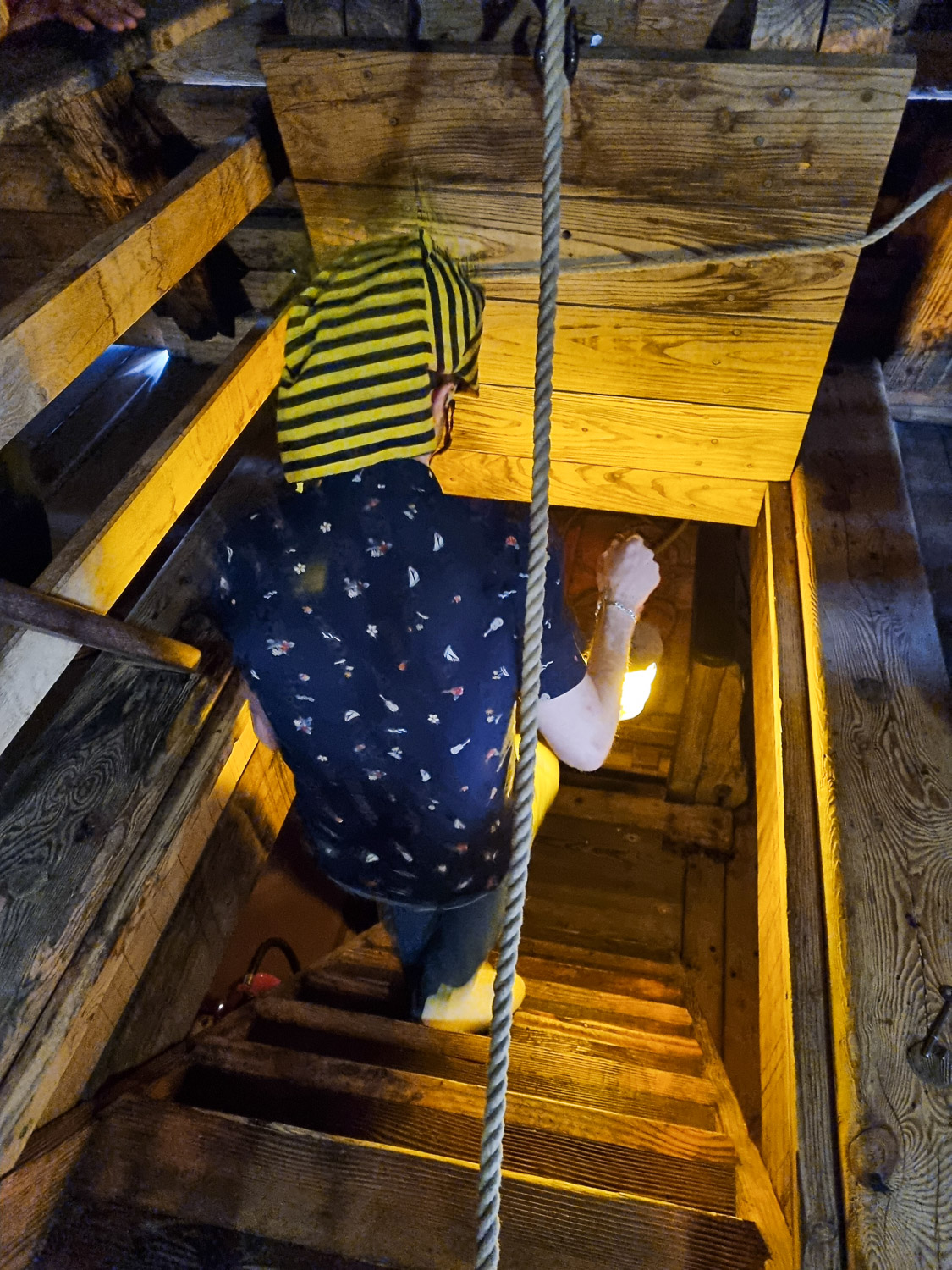 Man descending stairs through a hatch in the Golden Hinde ship, carrying a lantern - my Escape from the Golden Hinde review of a new escape room in London with kids