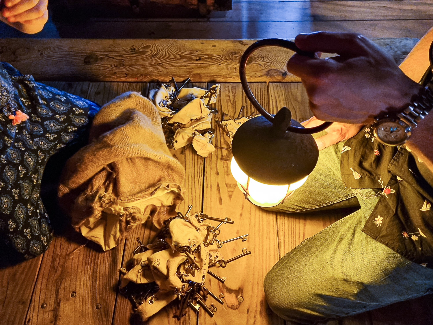 Adult and child's knees with a bag and piles of keys in the middle, illuminated by a lantern - my Escape from the Golden Hinde review of a new escape room in London with kids