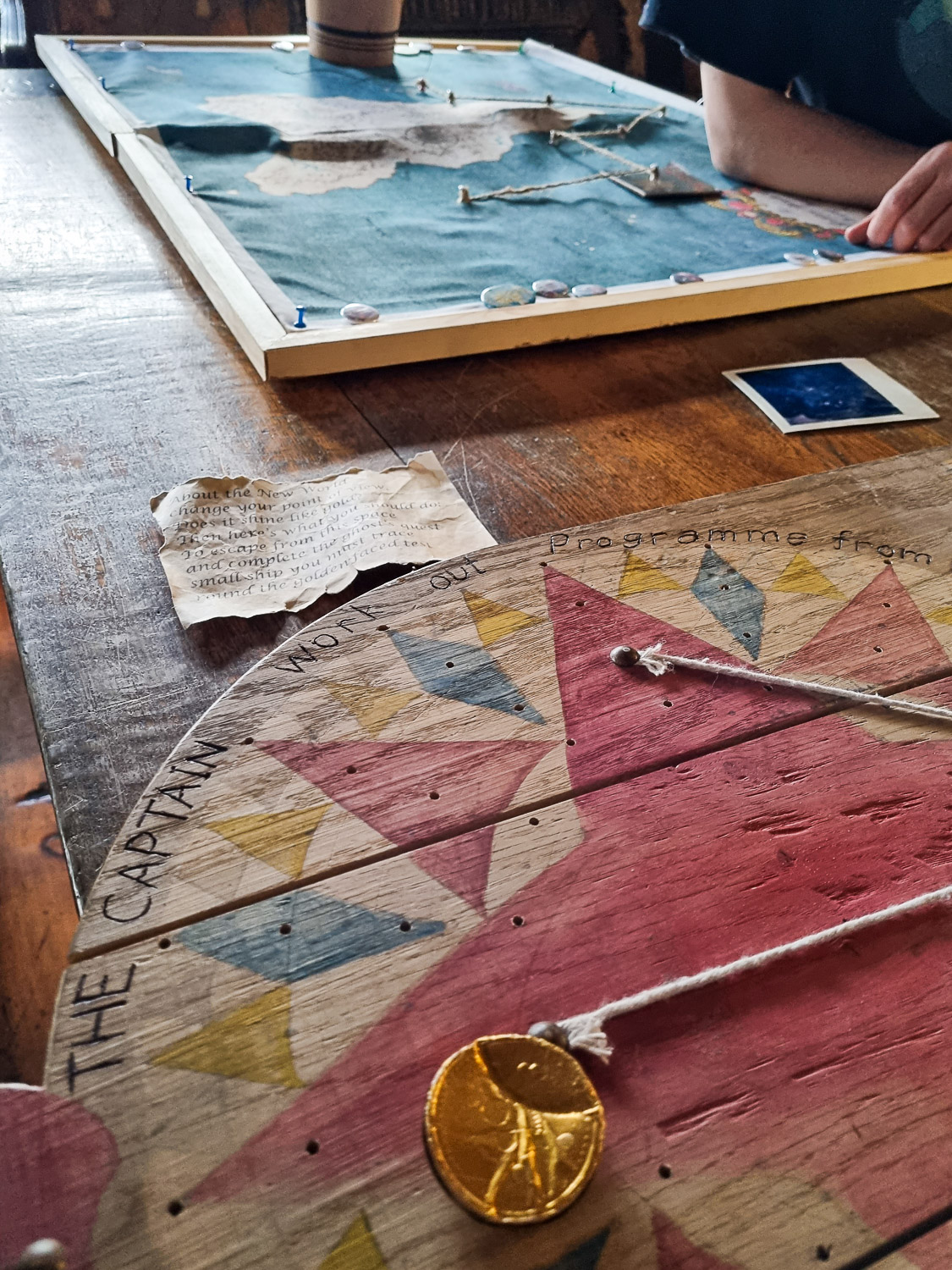 View across a table with board, map, paper, photo, and chocolate coin wrapper, some of the items as part of the Golden Hinde escape room game in London - my Escape from the Golden Hinde review