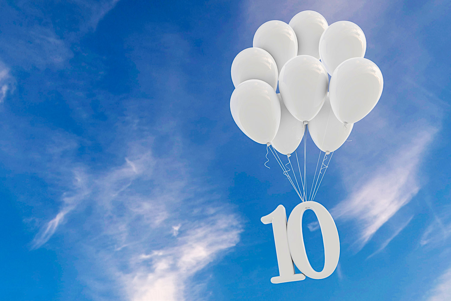 A bunch of white balloons against a blue sky with the number 10 suspended underneath - looking back on 10 years of family travel, and my latest experiences of travel with kids