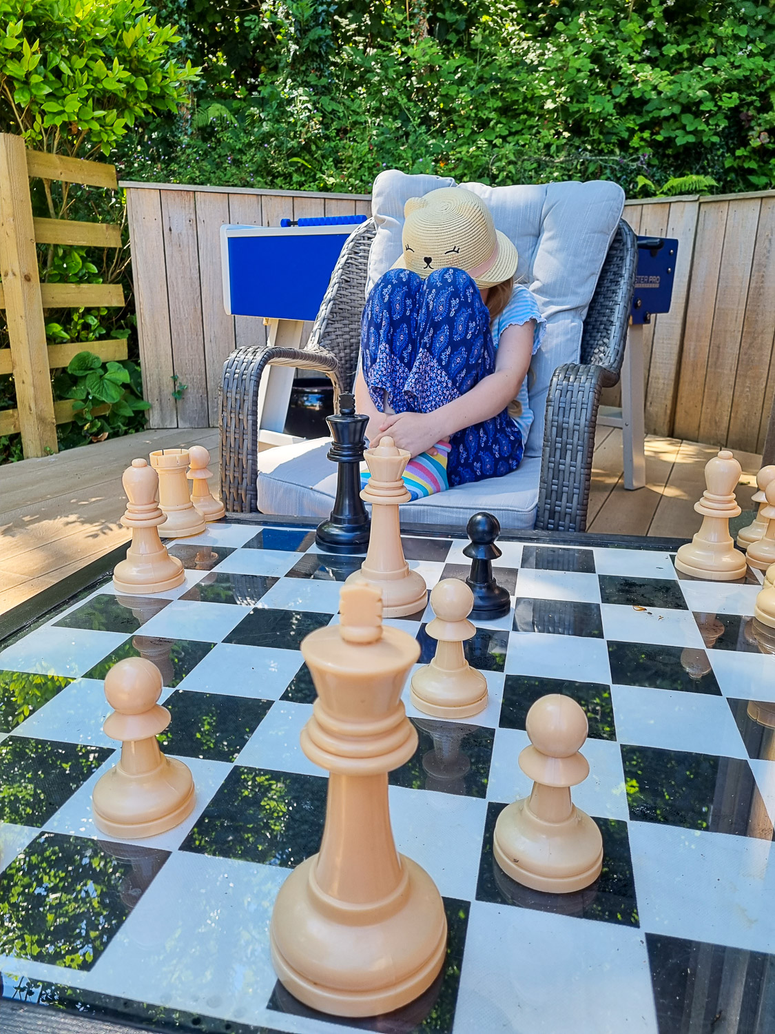 My daughter curled up in a chair across the outdoor chess set table - a stay at Dittisham Hideaway with kids
