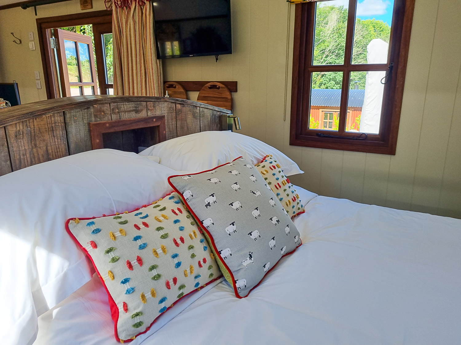 Bed with colourful cushions, looking towards the window, in one of the shepherd's huts at Dittisham Hideaway - my review of the Devon luxury glamping site