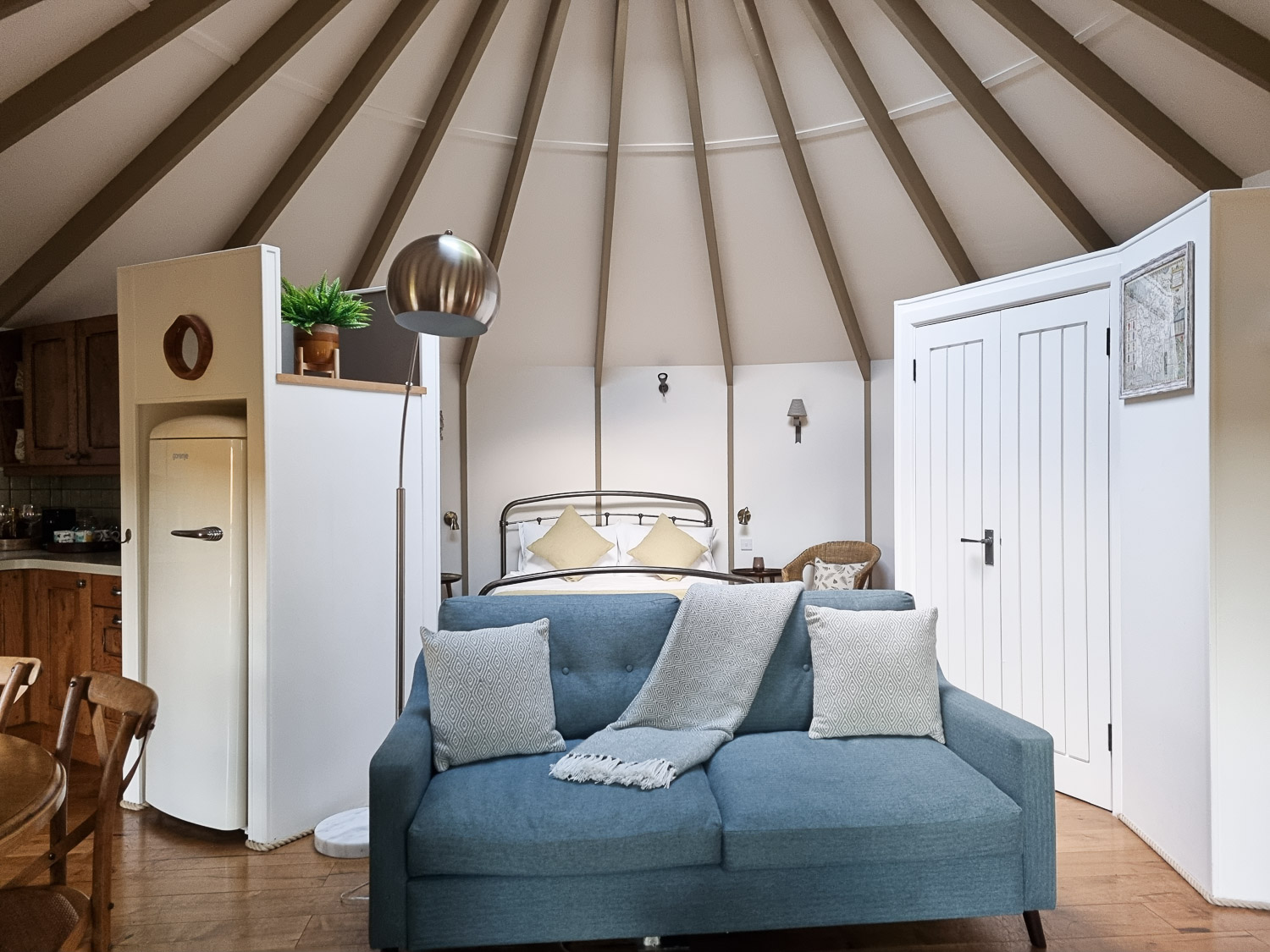 View of the interior of Owl treehouse looking across the armchair to the bed, with the fridge and white cupboard doors visible until a wood beamed tent style roof - my Dittisham Hideaway review after a stay at the Devon luxury glamping site