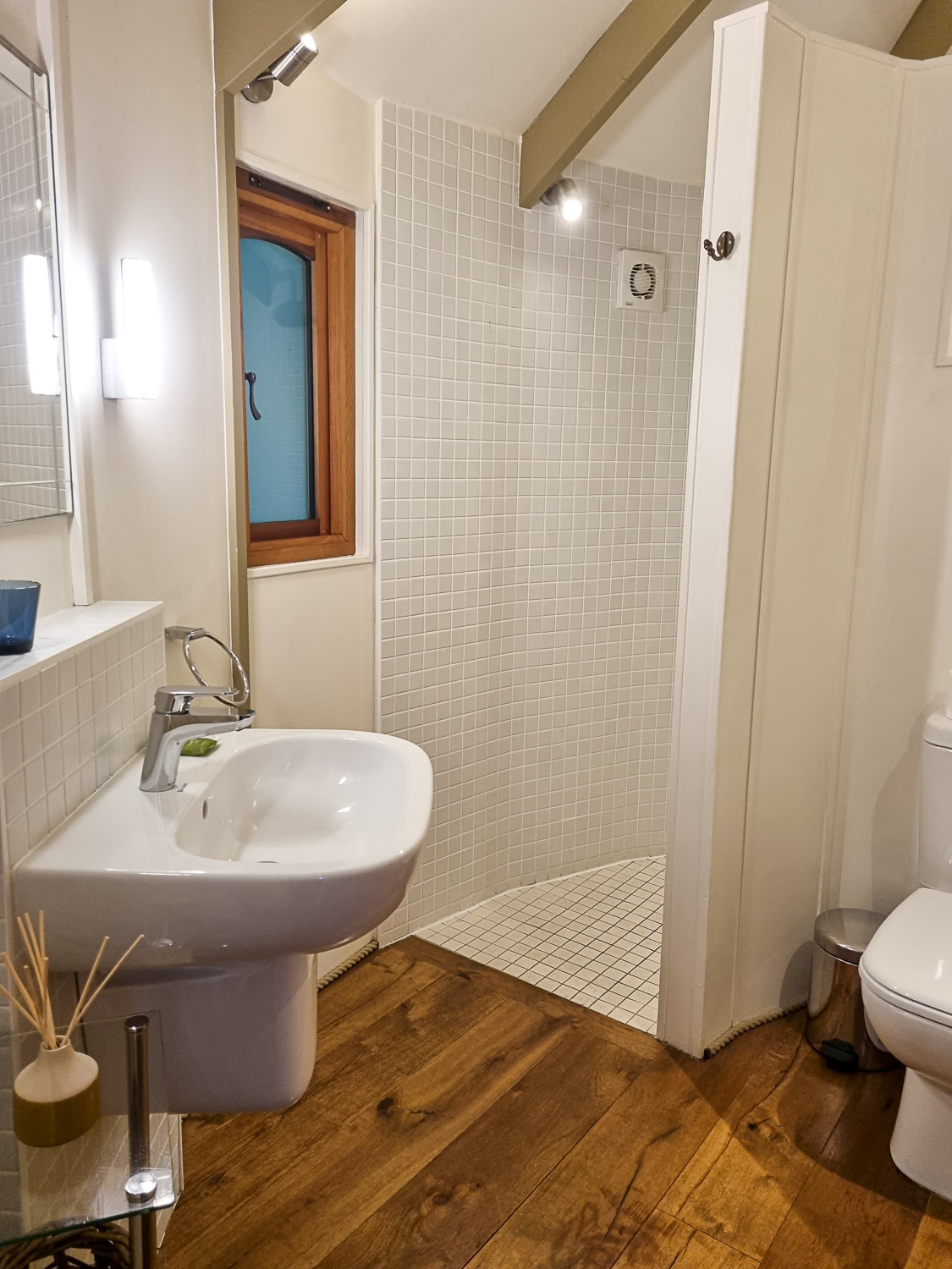 View across one of the bathrooms at owl treehouse, with white toilet partially seen, sink and pale tiled shower beyond - my Dittisham Hideaway review