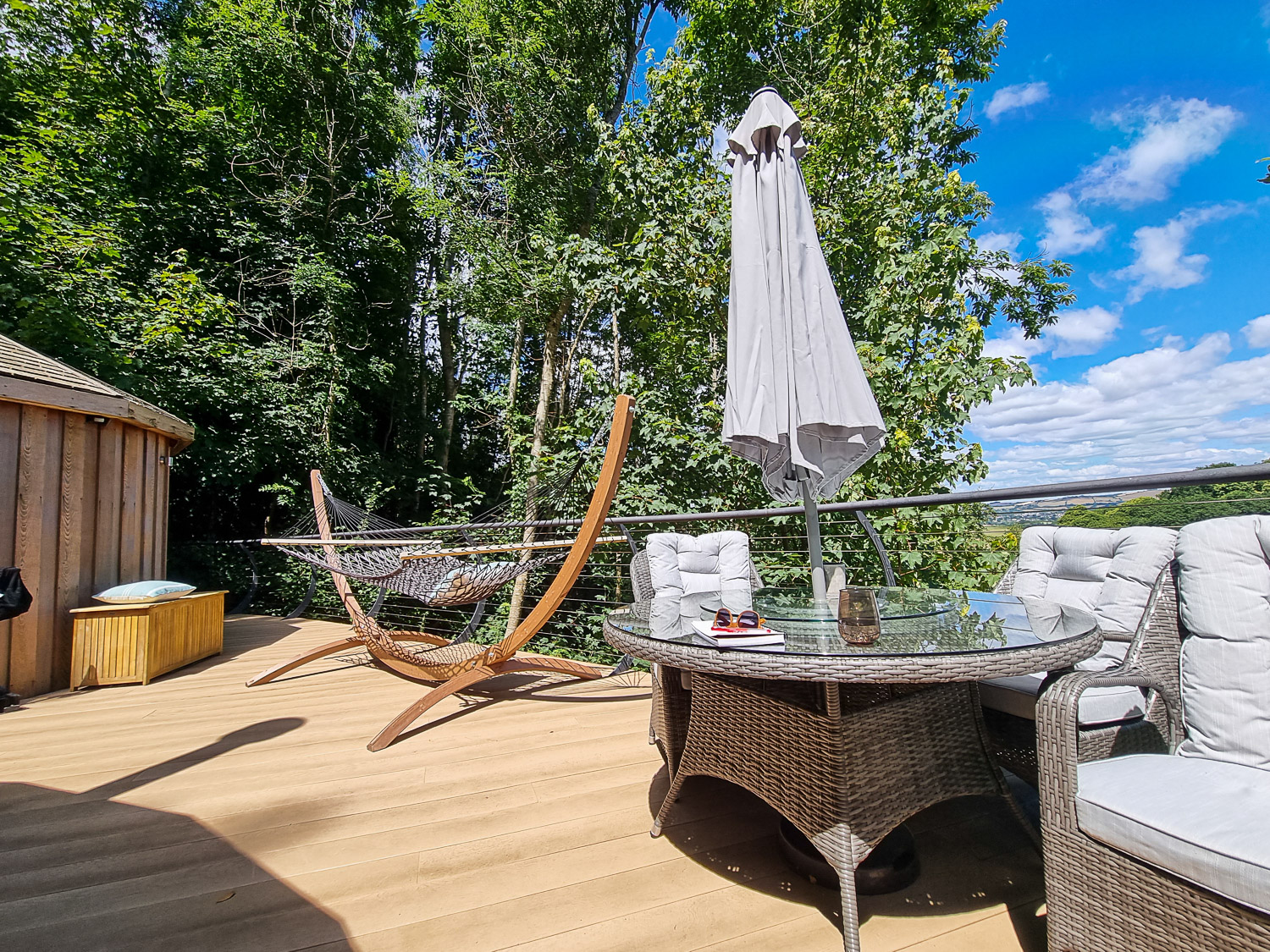 View past the outdoor table with parasol towards the hammock on a sunny day at Owl treehouse - my Dittisham Hideaway review