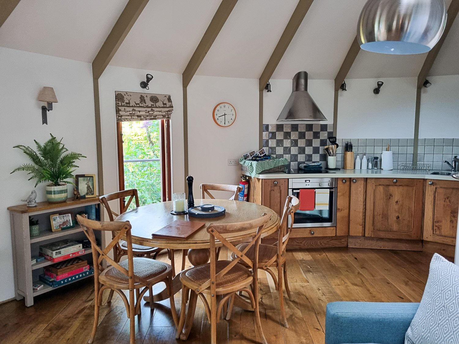 View across the wooden dining table to part of the kitchen at owl treehouse with oven and cupboards beyond - my Dittisham Hideaway review
