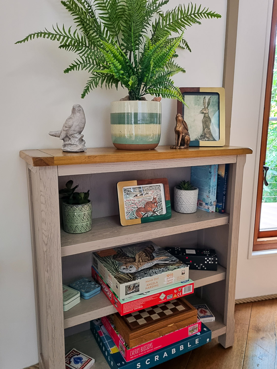 Bookcase with board games, puzzles and decorative touches including a fern in a ceramic pot - ideal for a stay at Devon's Dittisham Hideaway with kids
