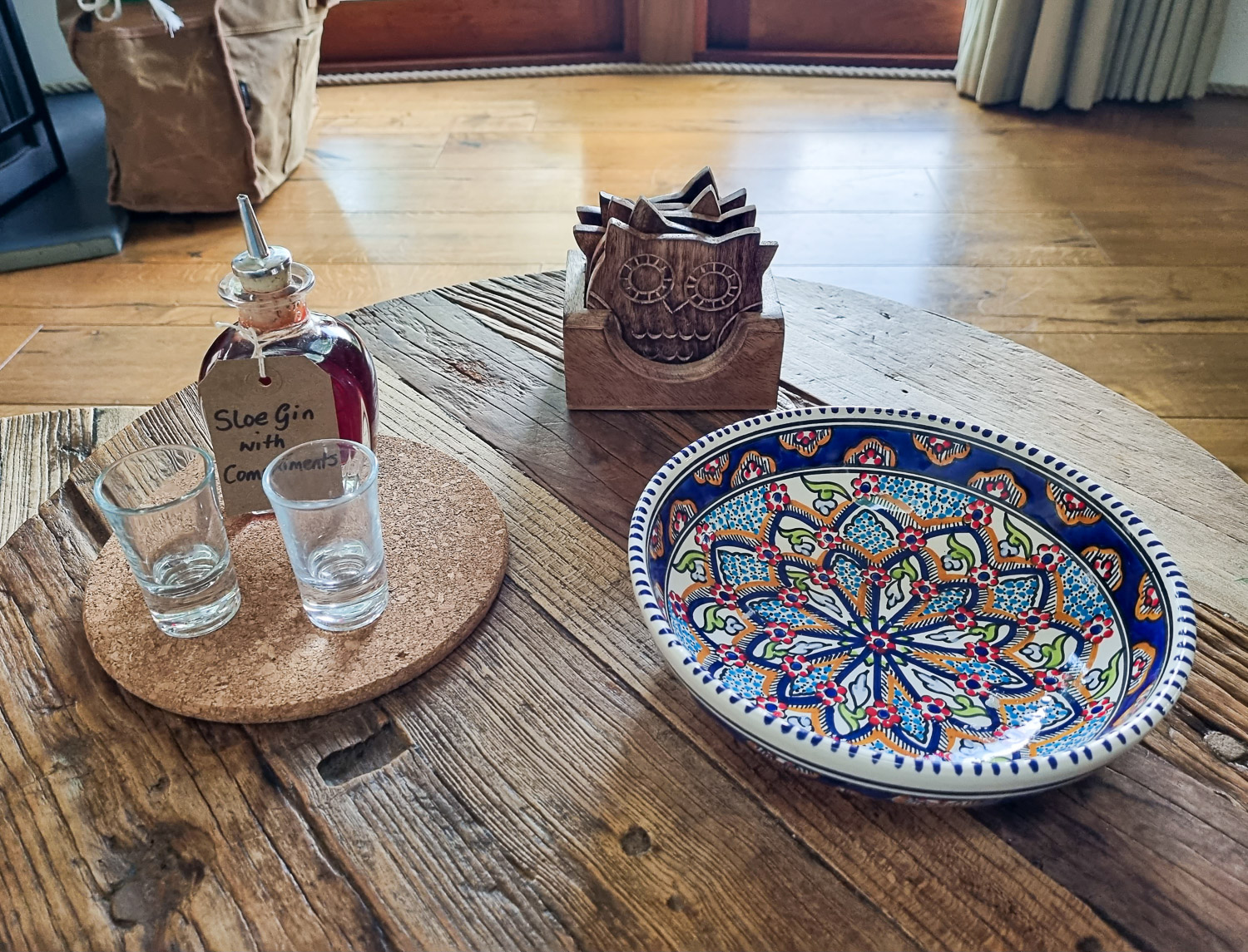 View of a north African-style patterns bowl and small bottle of complimentary sloe gin with shot glasses on a table in Owl treehouse - my Dittisham Hideaway review after a luxury glamping break in Devon