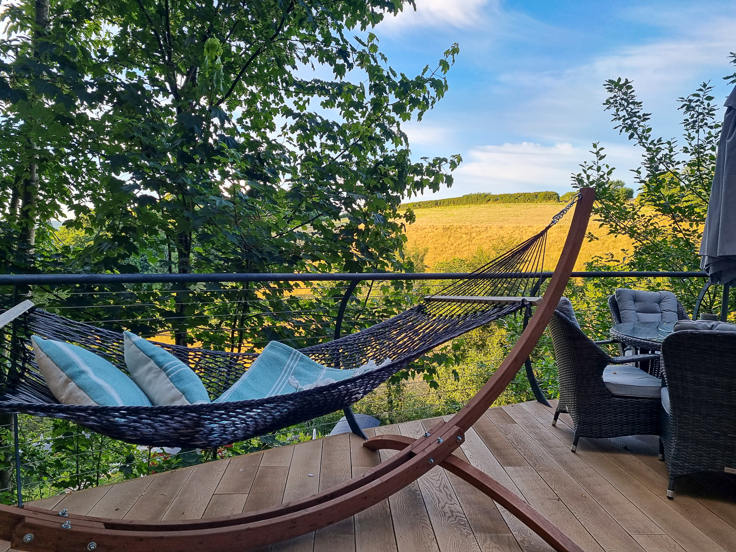 View across the hammock on the deck and outdoor table to the golden fields in Devon - my review of Dittisham Hideaway with kids