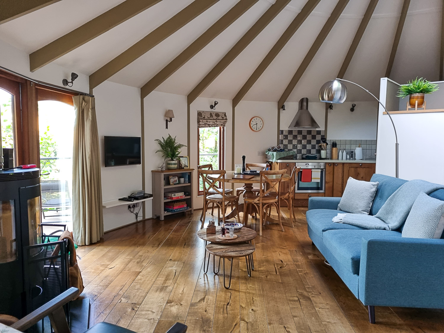 View of the interior of Owl Treehouse, including blue sofa, wooden dining table, TV and kitchen beyond - a review of Dittisham Hideaway luxury glamping in Devon