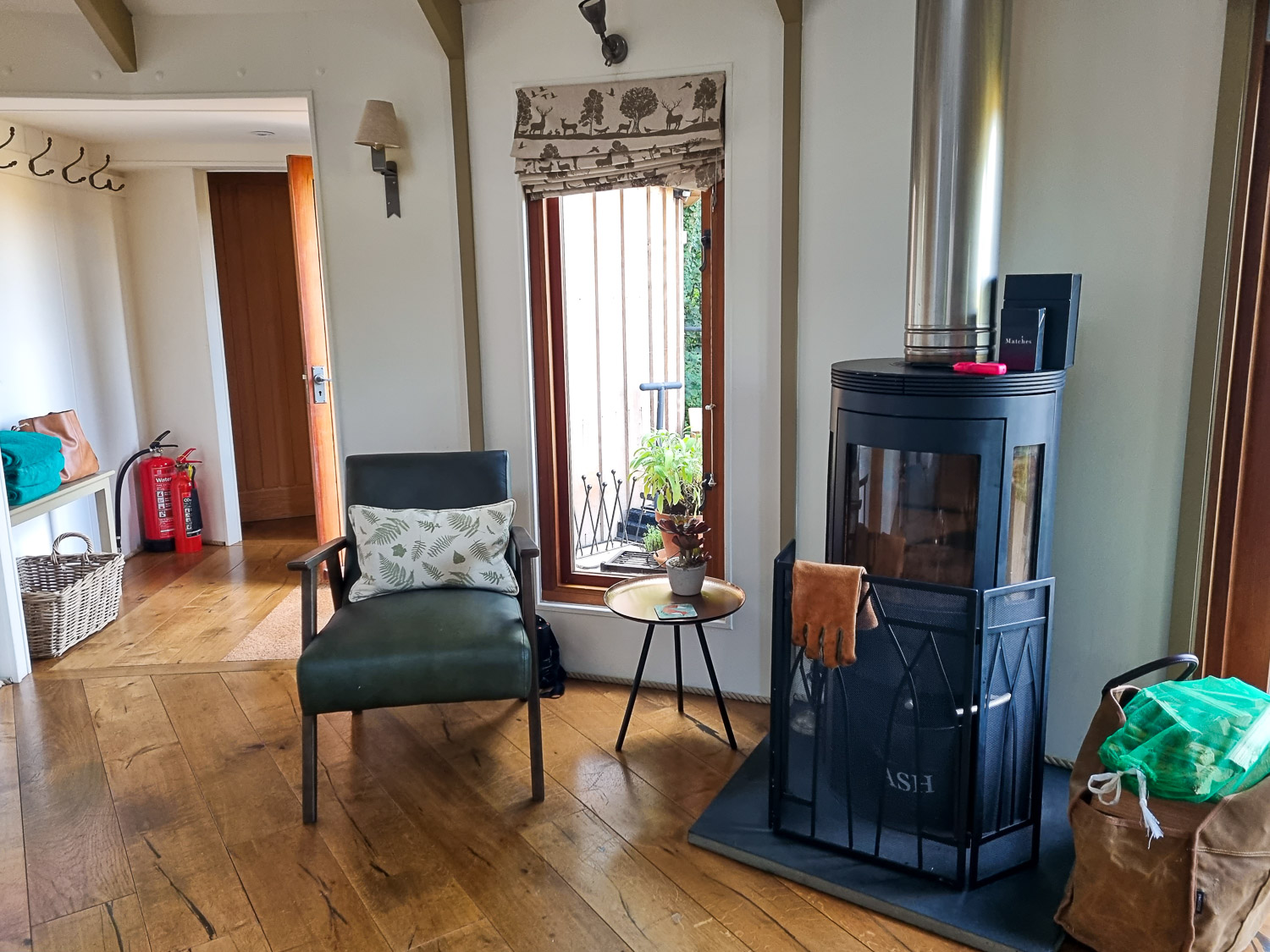 View towards the wood-fired stove, bag of wood and chair looking towards the hallway of Owl Treehouse - my Dittisham Hideaway review after a stay at the Devon luxury glamping site