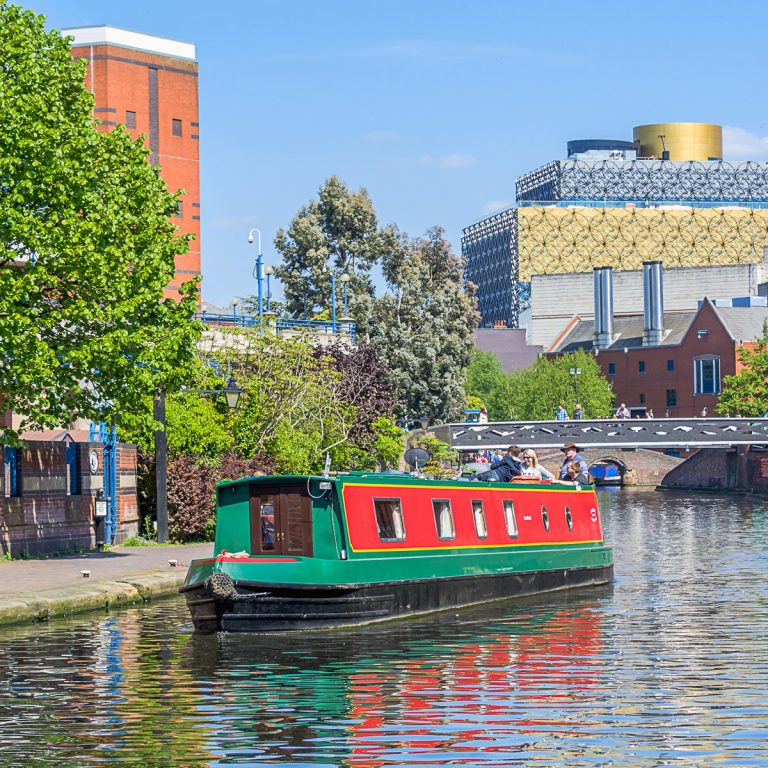 A red and green narrowboat on the canal in Birmingham with the cube and Sea Life Centre seen behind - my pick of the best things to do in Birmingham with kids