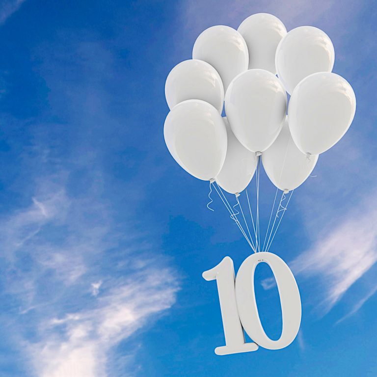 A bunch of white balloons against a blue sky with the number 10 suspended underneath - looking back on 10 years of family travel, and my latest experiences of travel with kids