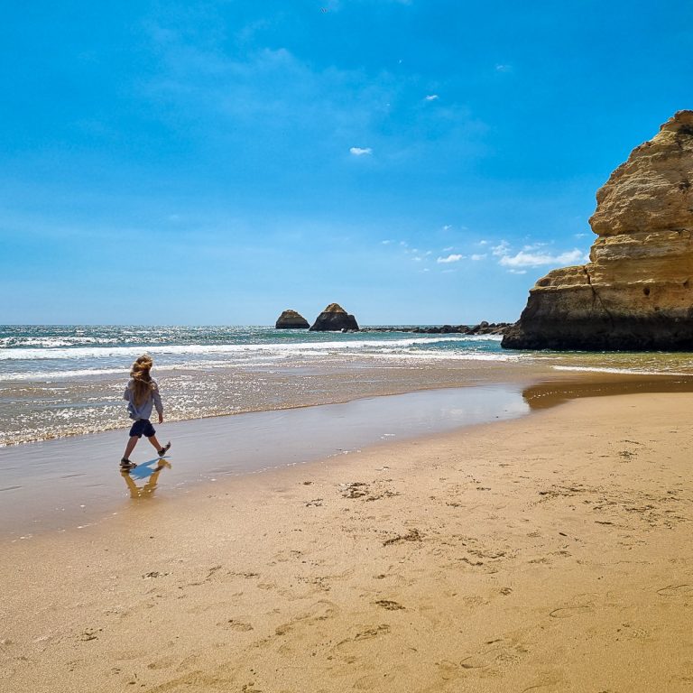 Girl walks along the sand towards the rocks of Praia da Rocha in Portimao on the Algarve - my guide to Portugal with kids