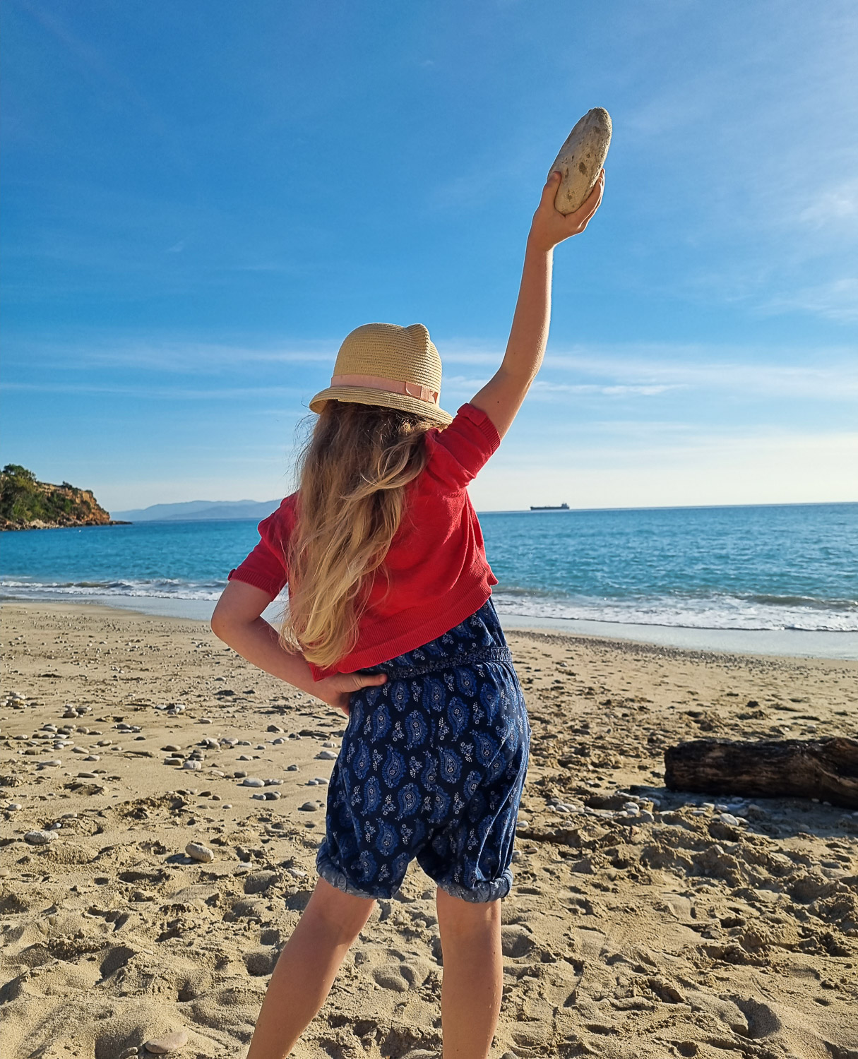 My daughter brandishes a rock high in the air as she looks out to the sea from a beach in Kefalonia - looking back on the latest of our 10 years of family travel