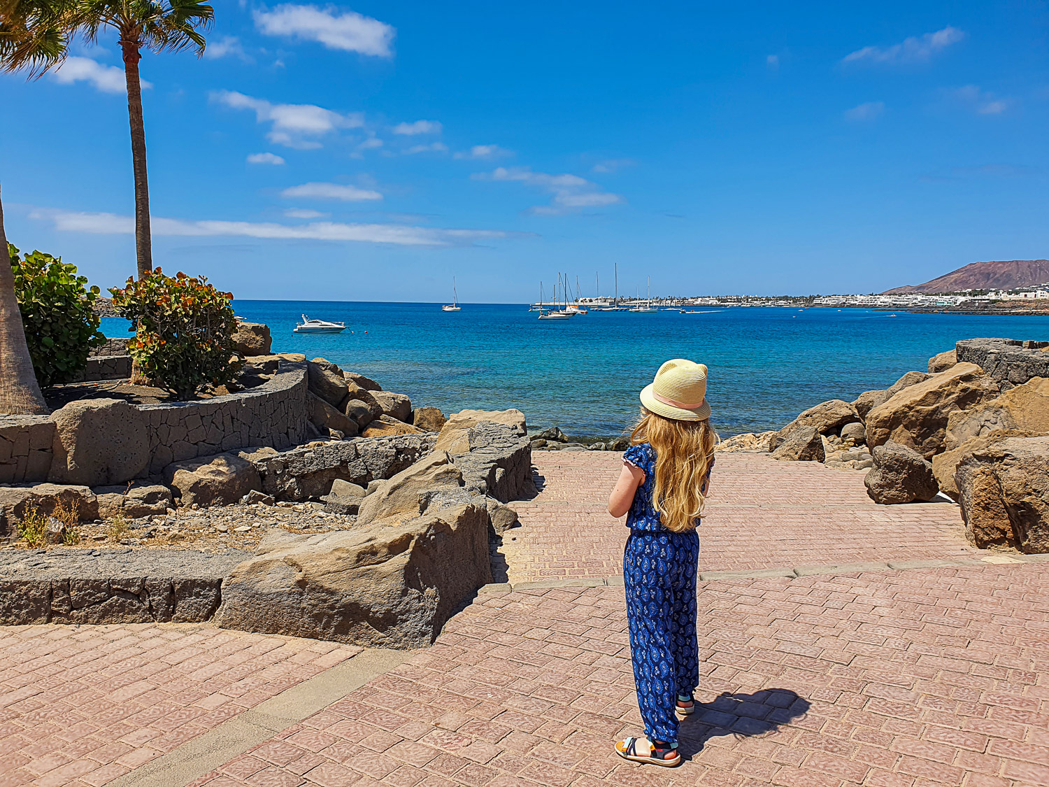 My daughter stands on the paved promenade by the seafront at Playa Blanca in Lanzarote - the destination for our first post-pandemic flight as I look back on 10 years of travel with a child
