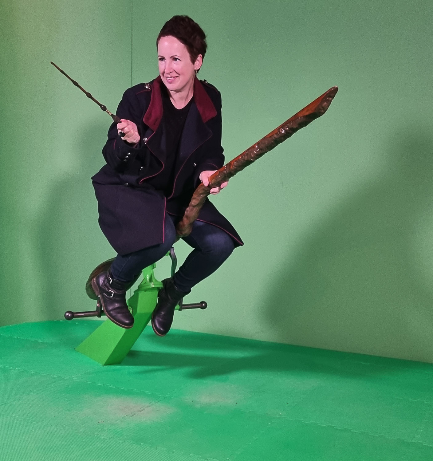 Photo of me sitting on a broomstick against green screen holding a prop wand for my review of the Harry Potter Photographic Exhibition in London