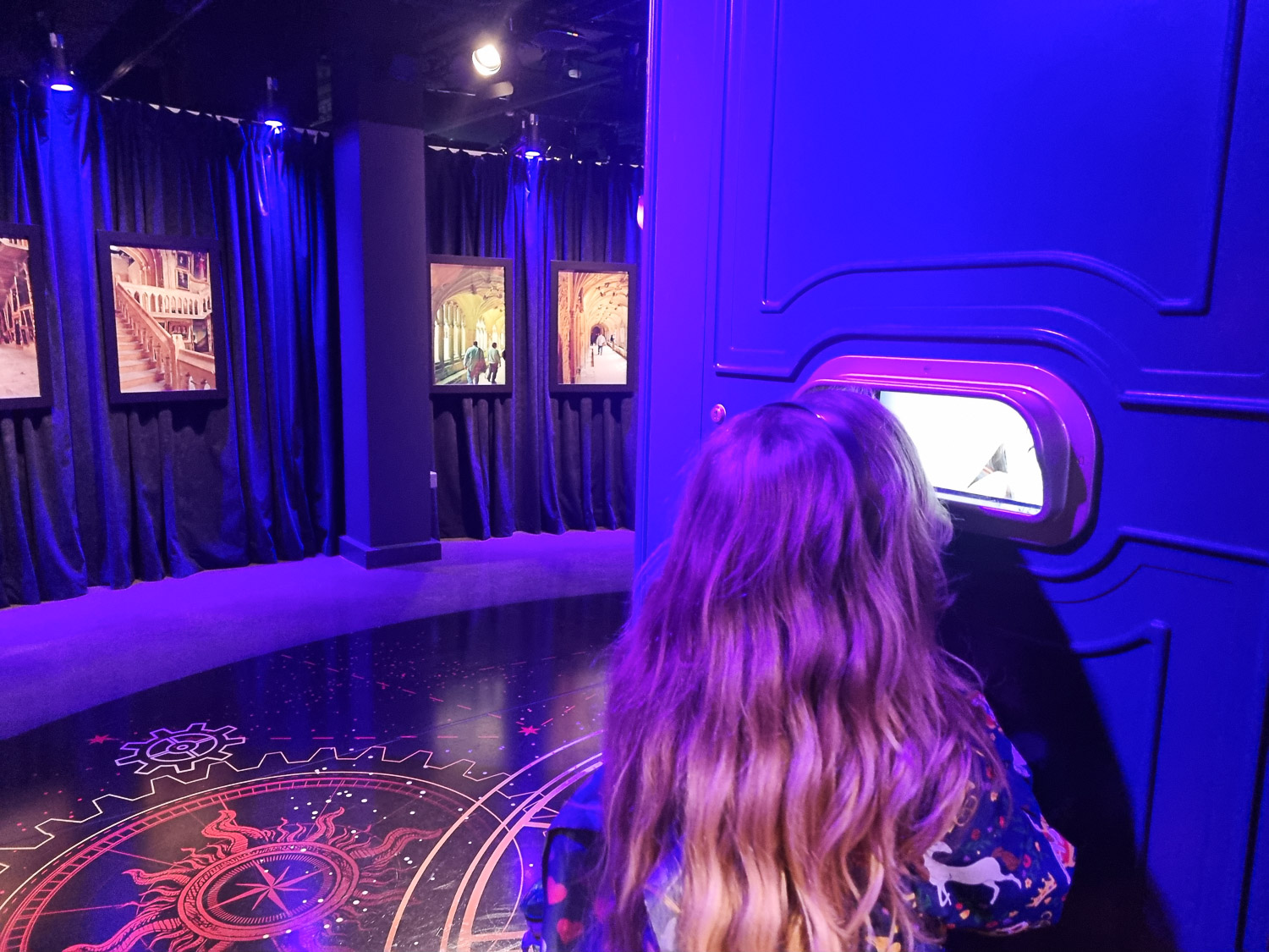 My daughter peers into an opening showing snippets of video as part of one of the displays during our visit to London's Harry Potter Photographic Exhibition with kids