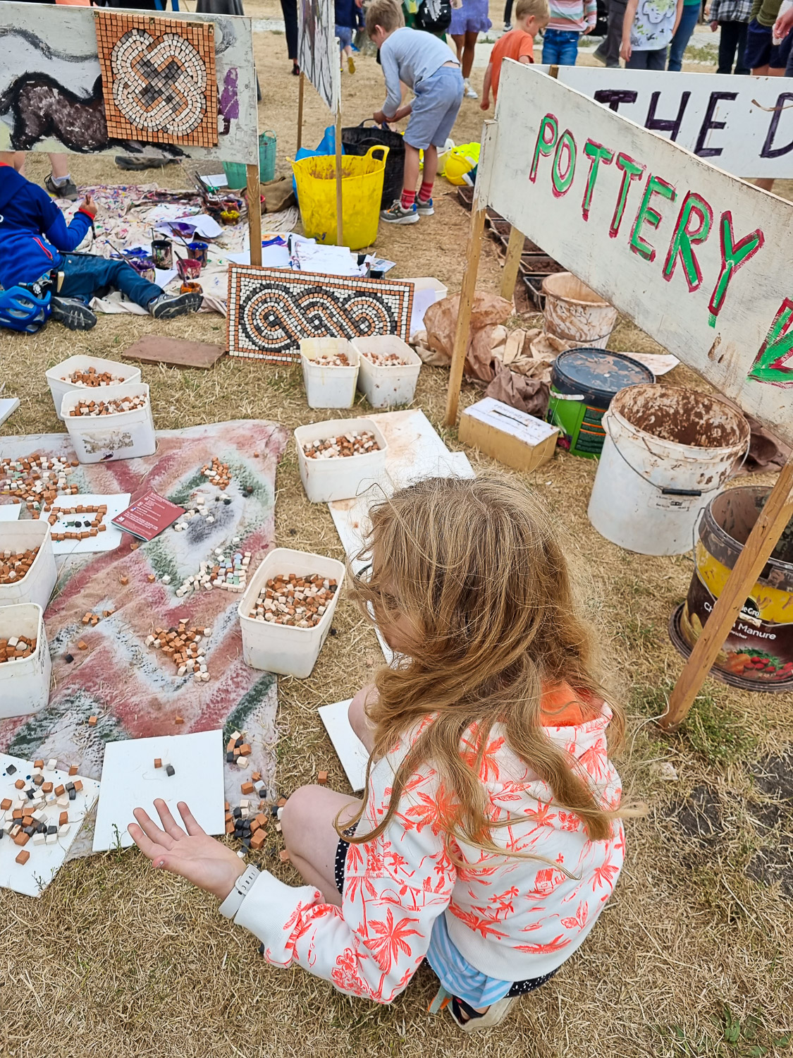 My daughter crouches next to tubs of mosaic pieces, one of the temporary activities taking place during a visit to Corfe Castle with kids