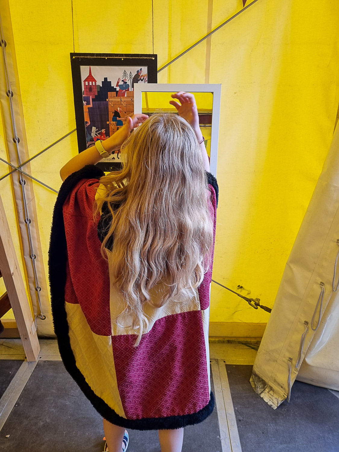 My daughter tries on medieval robes in front of a mirror in a tent as part of some of the temporary summer activities at Corfe Castle for kids
