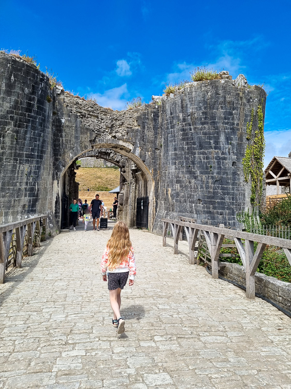 My daughter walks towards the entrance archway into Corfe Castle during a day out in Dorset with kids