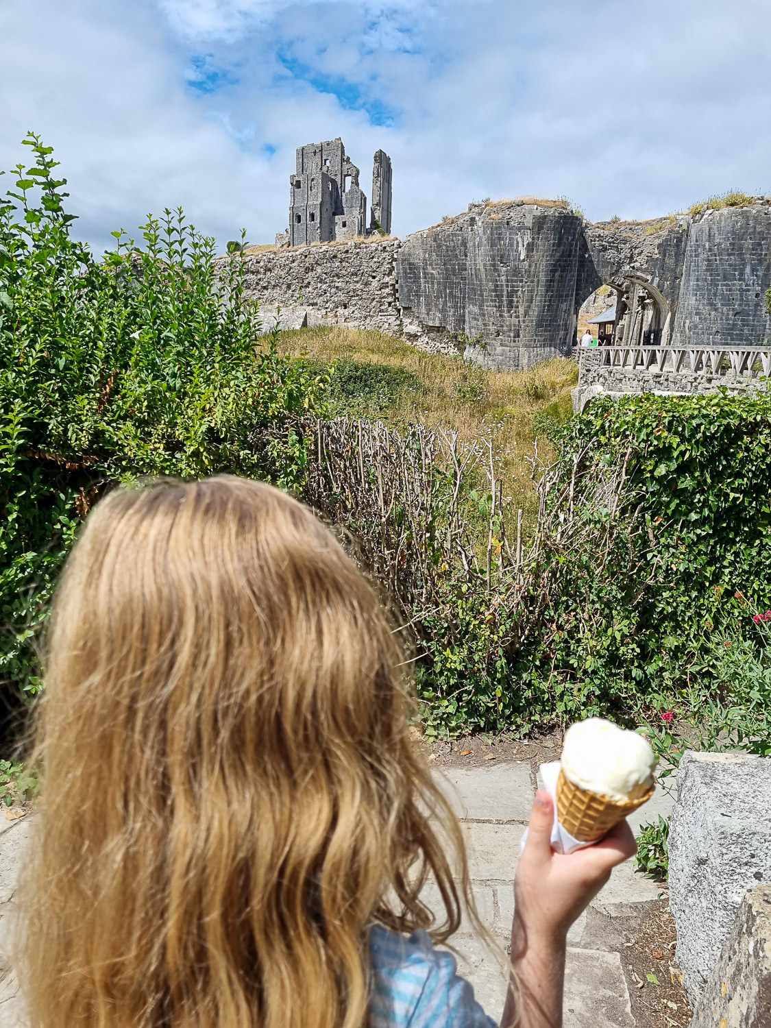 My daughter holds and ice cream in the National Trust tearoom, looking up towards the ruins during a day out at Corfe Castle with kids