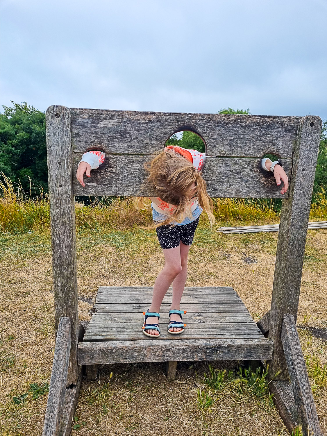 My daughter hangs her head while in the old wooden stocks at Corfe Castle