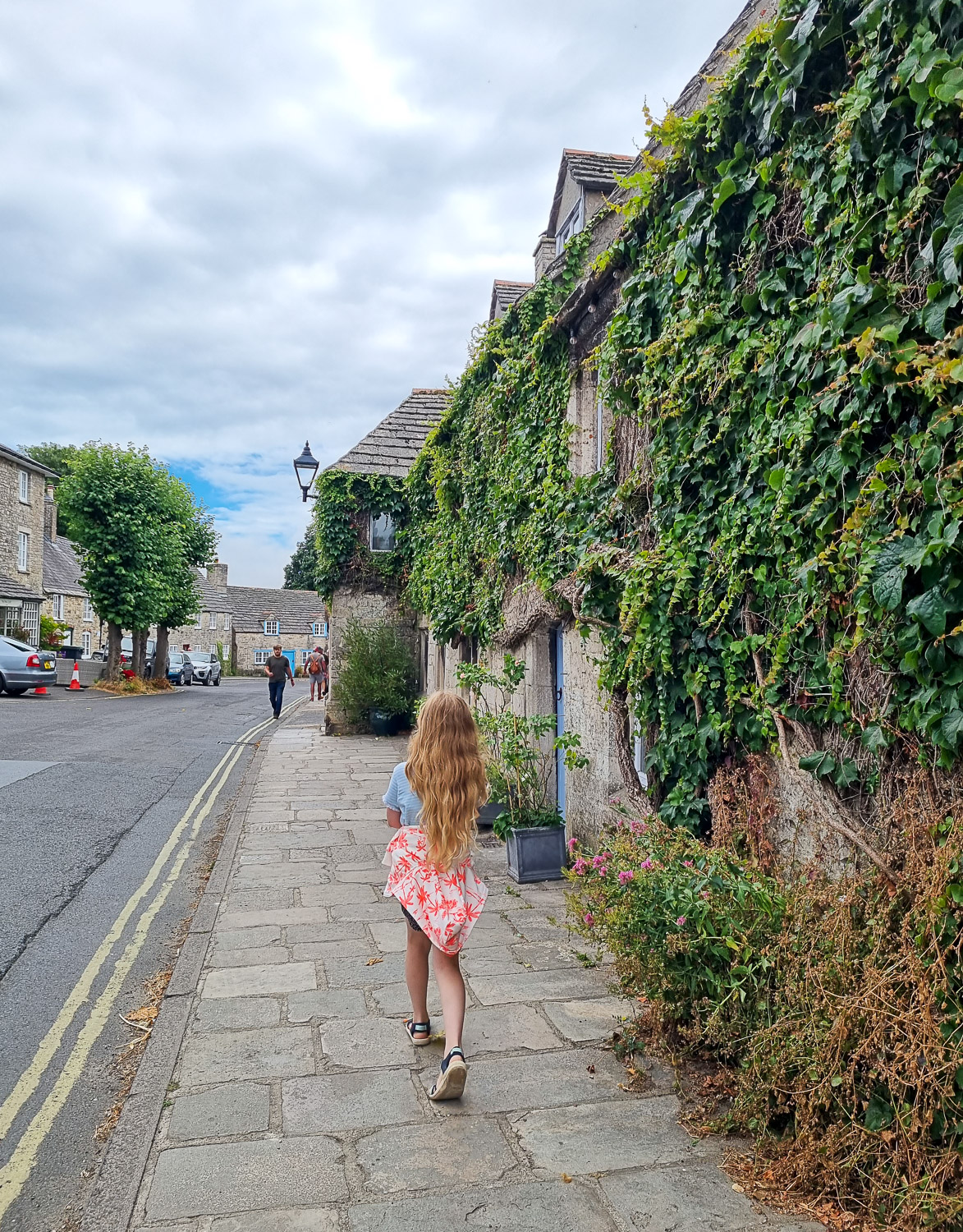 My daughter walks through one of the old streets of Corfe with ivy covered stone houses - don't miss exploring the village if you're planning a day out at Corfe Castle with kids