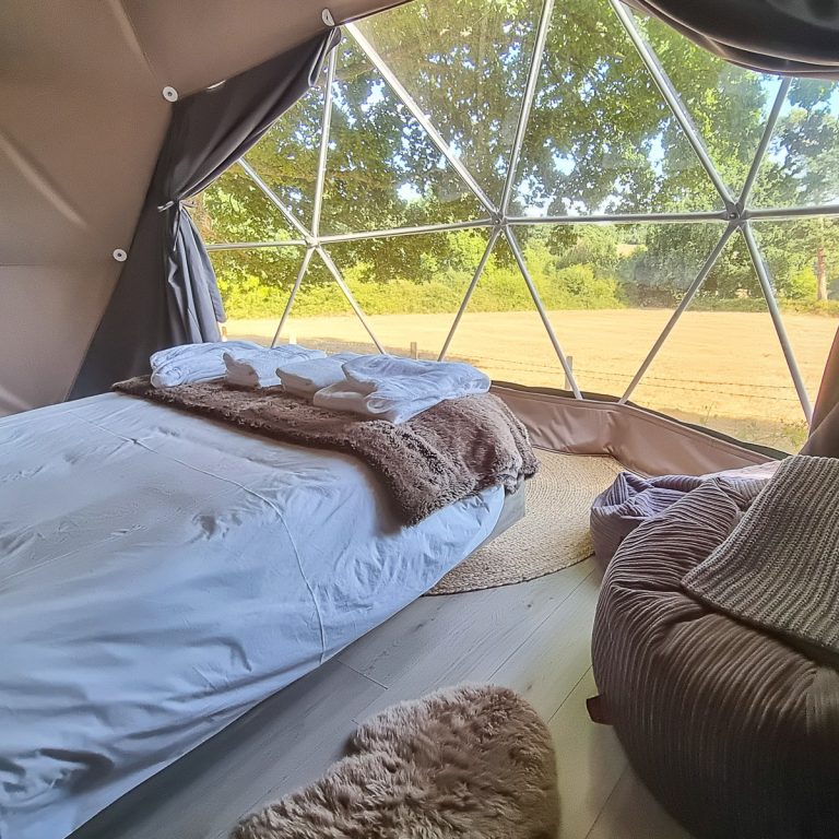 View of the interior of Knole Luna Dome with beanbags plus main bed, complete with furry throw and soft robes, plus window looking out to the fields beyond - my review of luxury glamping in Kent with kids