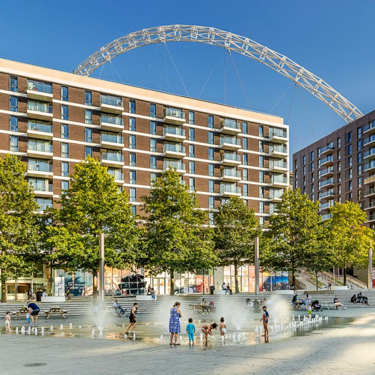 View of families in the square by the fountains, and the Wembley arch visible behind the buildings - my tips for the best things to do during a day at Wembley Park with kids