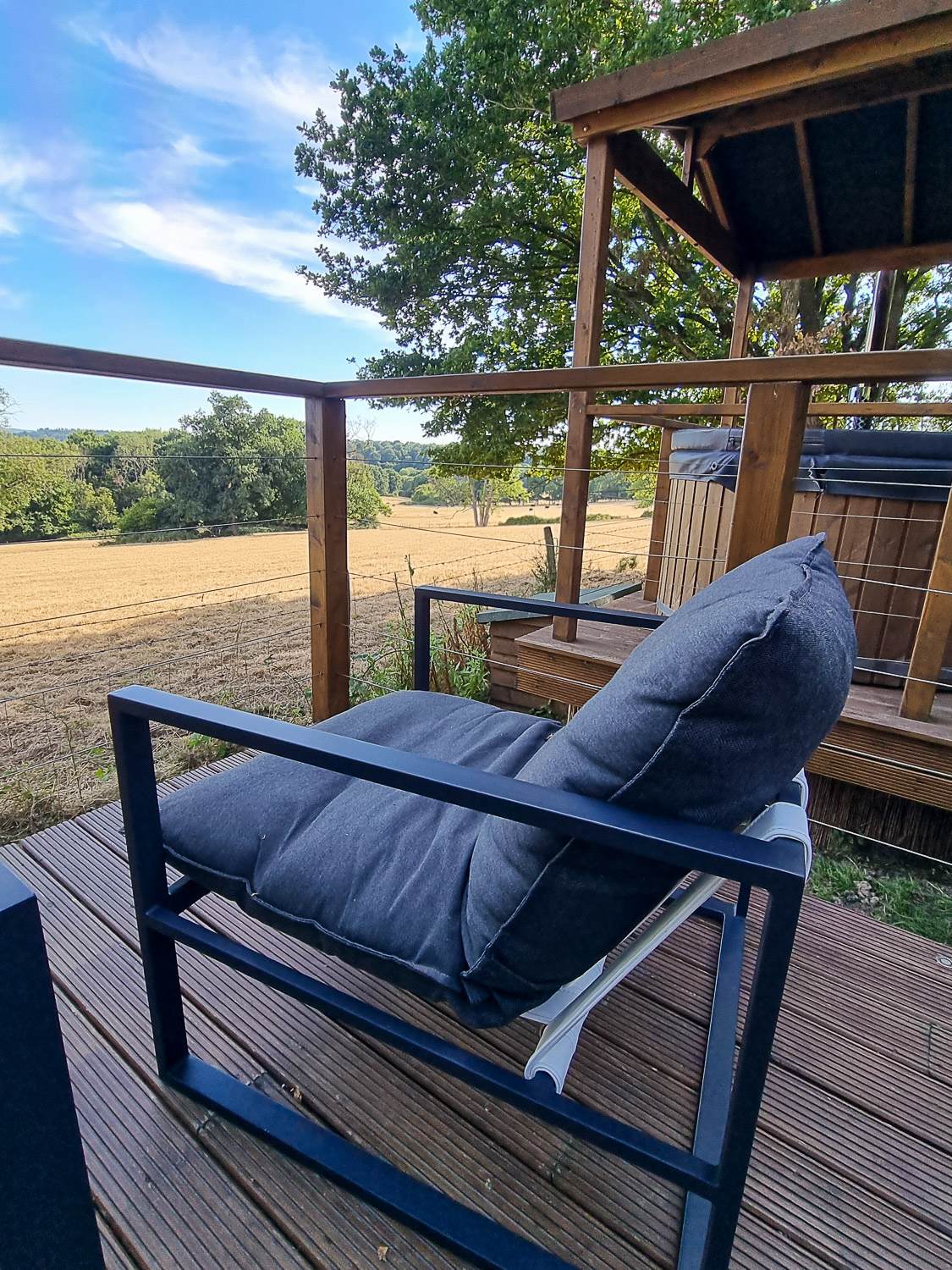 View of one of the comfy chairs on the deck at Knole Luna Dome, with the field and hot tub visible - my review of luxury glamping in Kent with kids at Hoath House