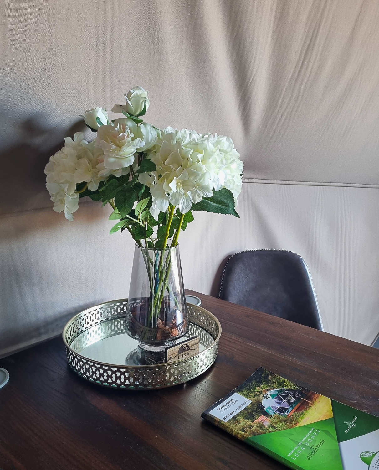 Small indoor table at Knole Luna Dome with vase of artificial white flowers and guidebook - my review of luxury glamping at Hoath House in Kent with kids