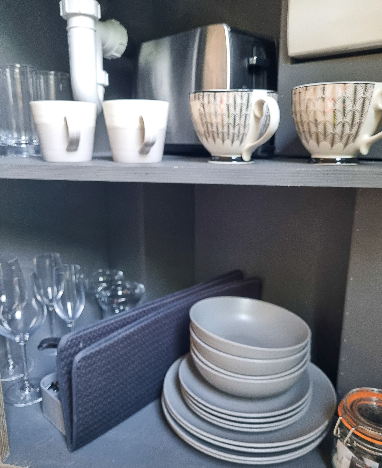 Crockery and glassware in the small cupboard of the kitchenette at Knole Luna Dome, tucked under the sink - my review of luxury glamping in Kent with kids