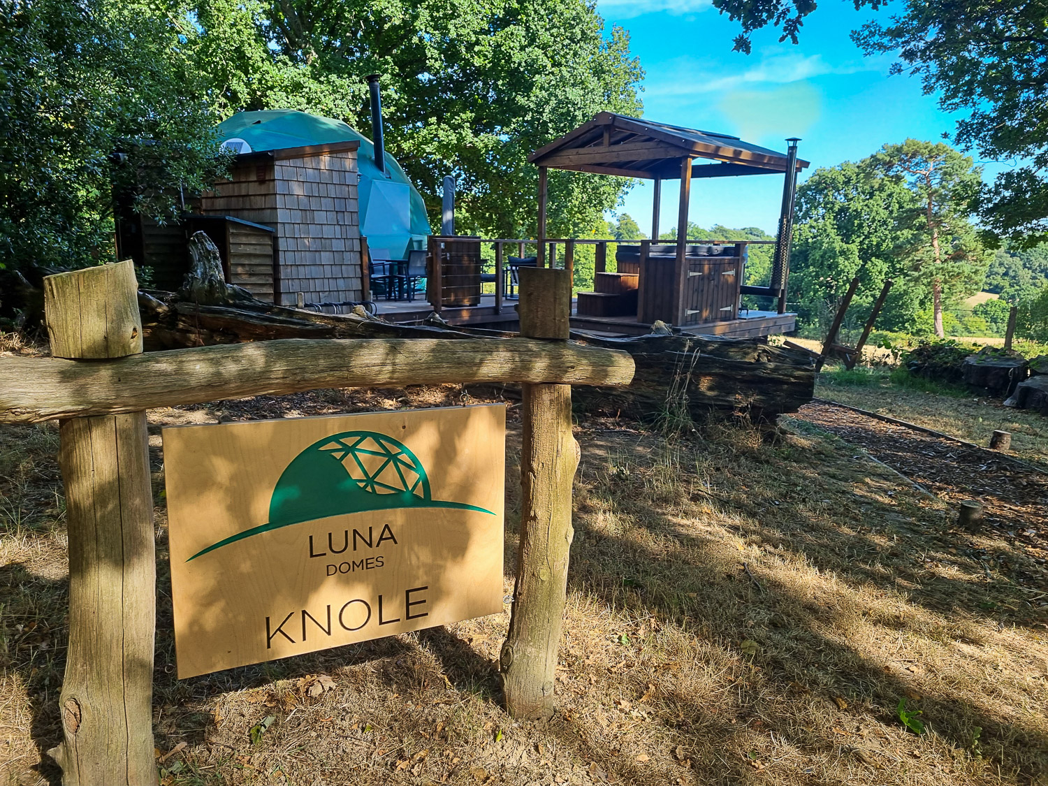 Sign for Knole Luna Dome with the deck, hot tub and dome itself visible beyond - my review of luxury glamping in Kent with kids