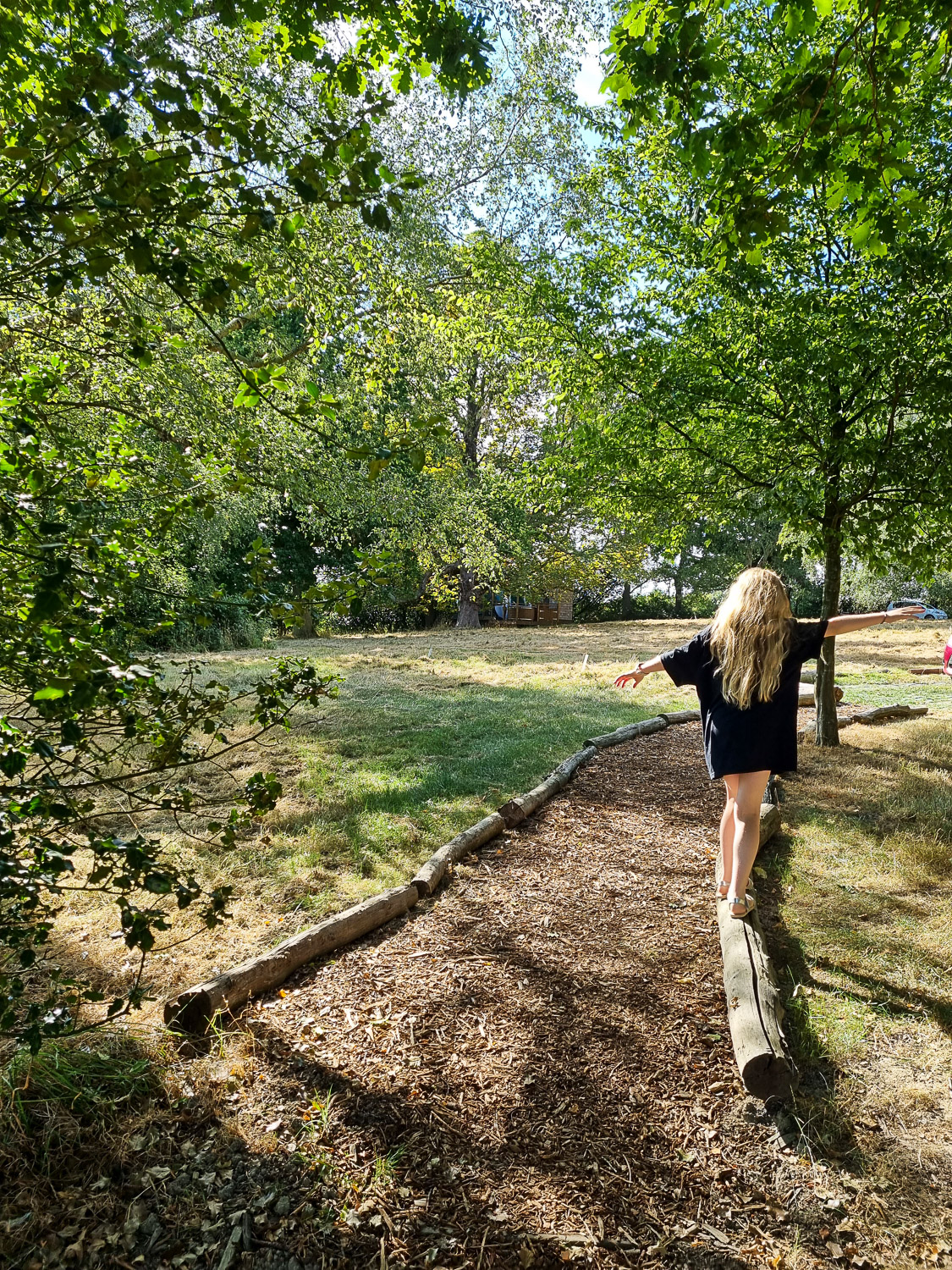 My daughter balances on the logs lining to path to Knole Luna Dome, secluded from the other accommodation at Hoath House - my review of luxury glamping in Kent with kids