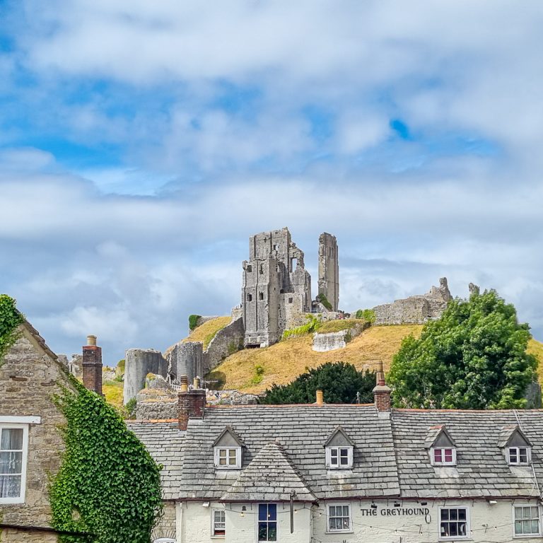 View from Corfe up to the ruins of the castle on its hill over The Greyhound pub - things to do during a day out in Dorset at Corfe Castle with kids