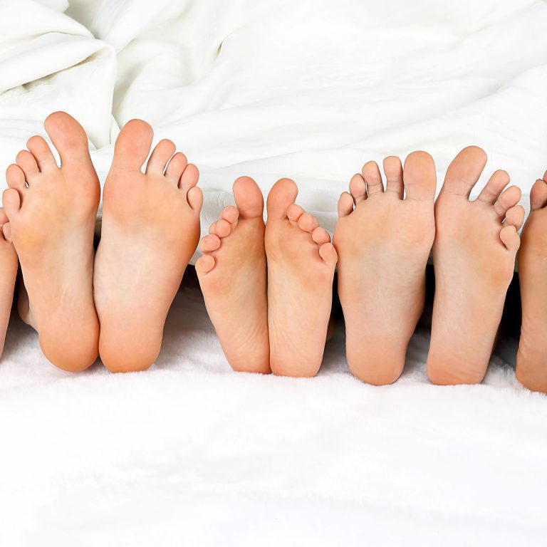 Bed showing row of five pairs of adult and child feet peeking out from under white bedlinen - if you're a bigger family, these are my tips on finding the best family hotels in London sleeping five