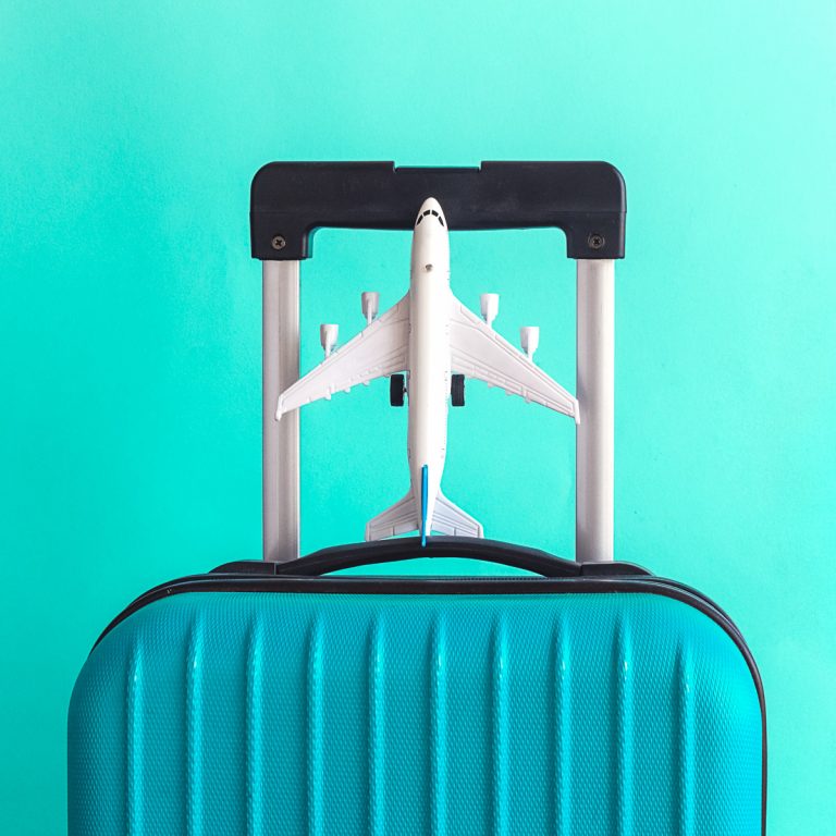 Suitcase and airplane model on pastel green background - if you're looking to travel from a London airport to central London, these are my tips on the best options using public transport