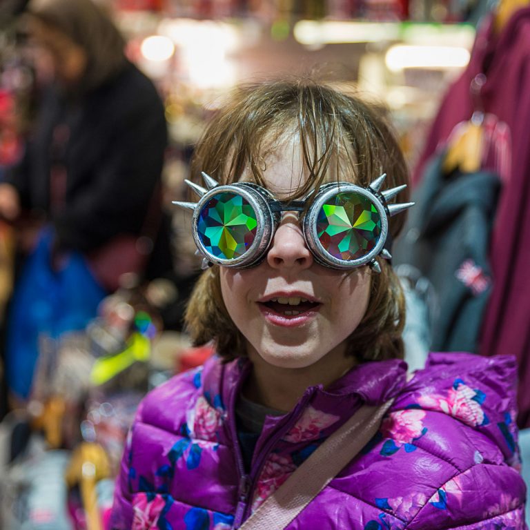 Young girl with kaleidoscope style steampunk sunglasses in front of clothes on sale in Camden - finding the best things to do in Camden with kids and teens
