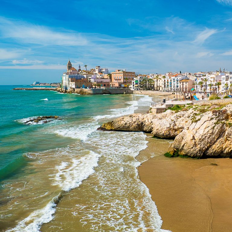 View along the coast and beaches towards the white and ochre buildings of the Spanish town - my pick of the best things to do in Sitges with kids
