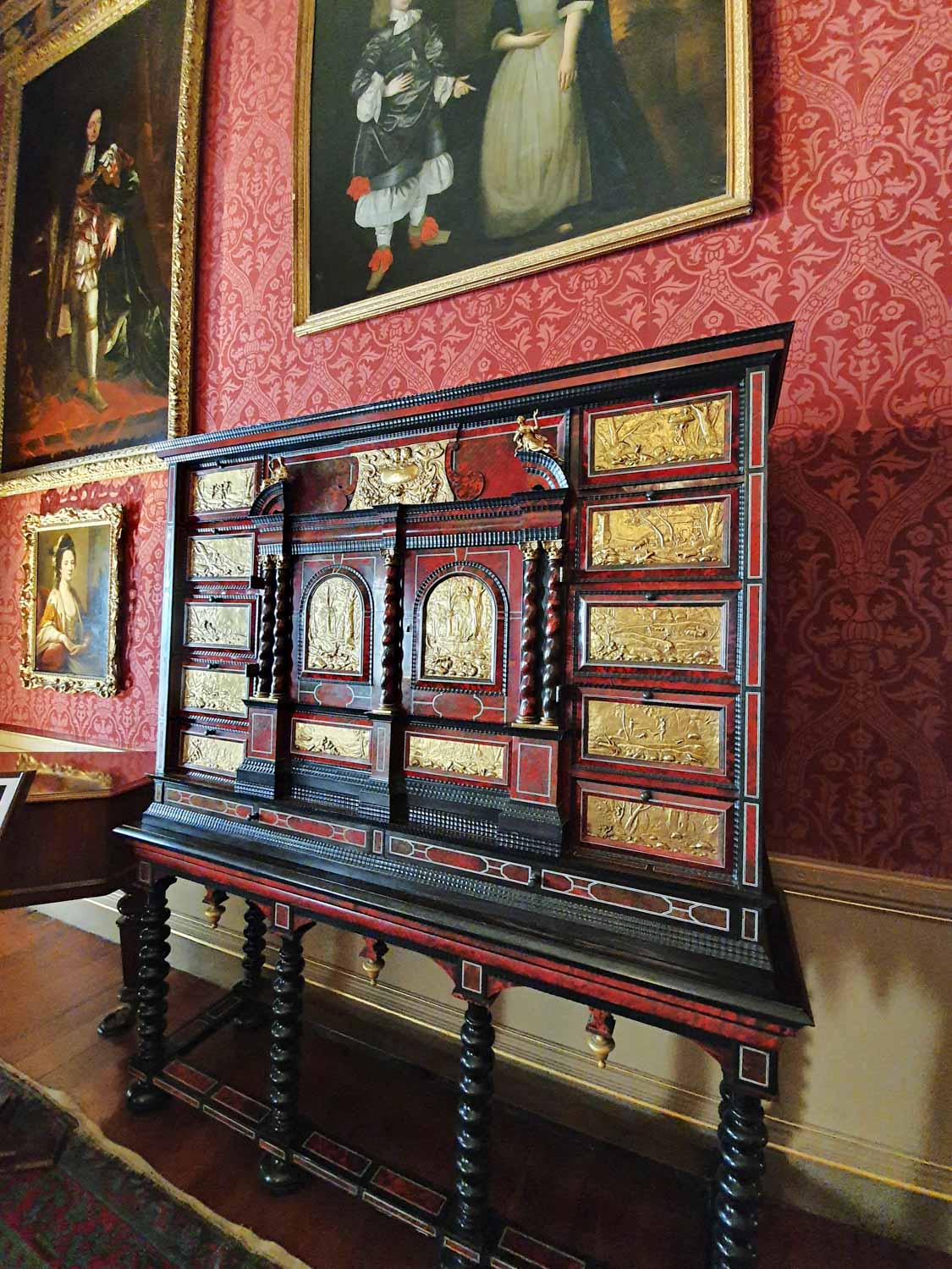 Gold inlaid furniture against red wallpaper with portraits - a day out at Oxburgh Hall in Norfolk with kids
