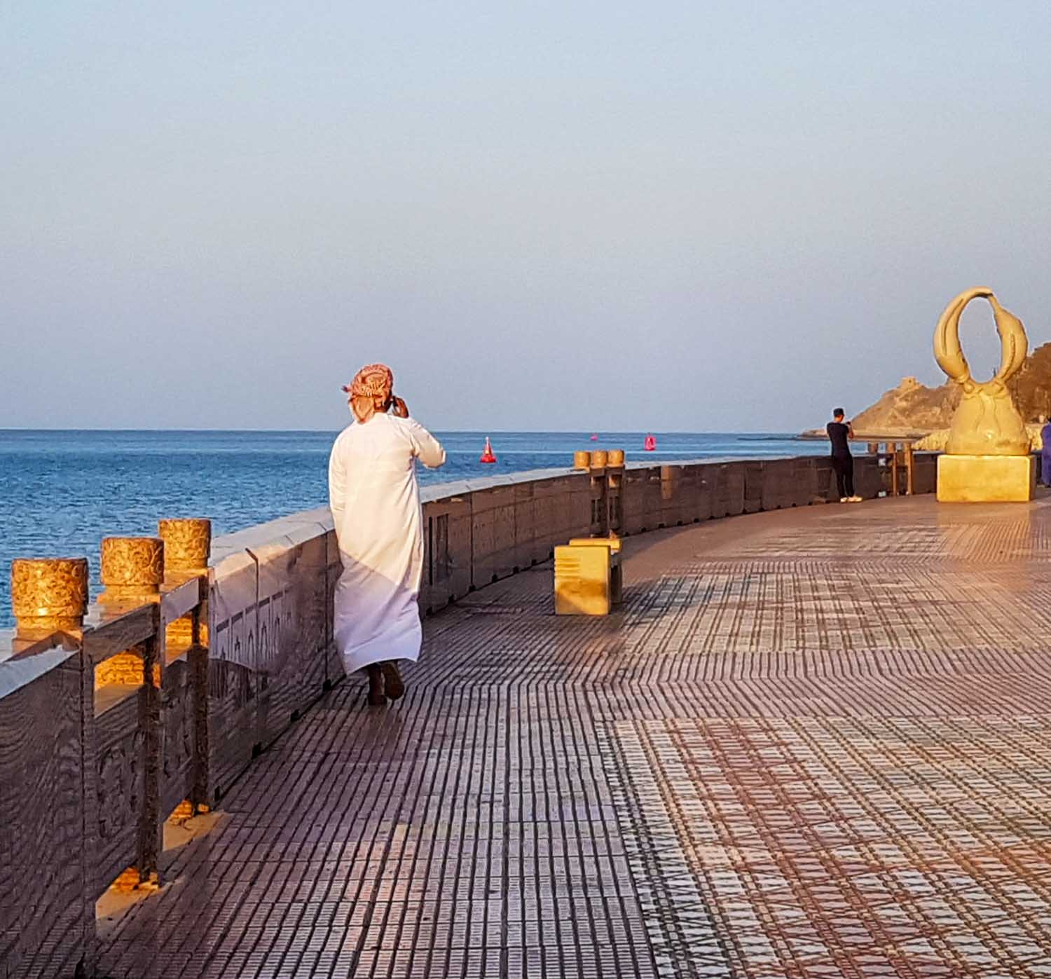 A man in white dishdasha and masar turban walks along the corniche at Mutrah at sunset in Muscat, Oman - my nine reasons to visit Oman with kids