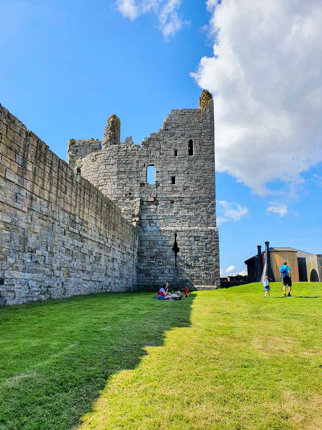 View along the grassy court and wall to a ruined tower at Dunstanburgh Castle in Northumberland - visiting Dunstanburgh Castle with kids