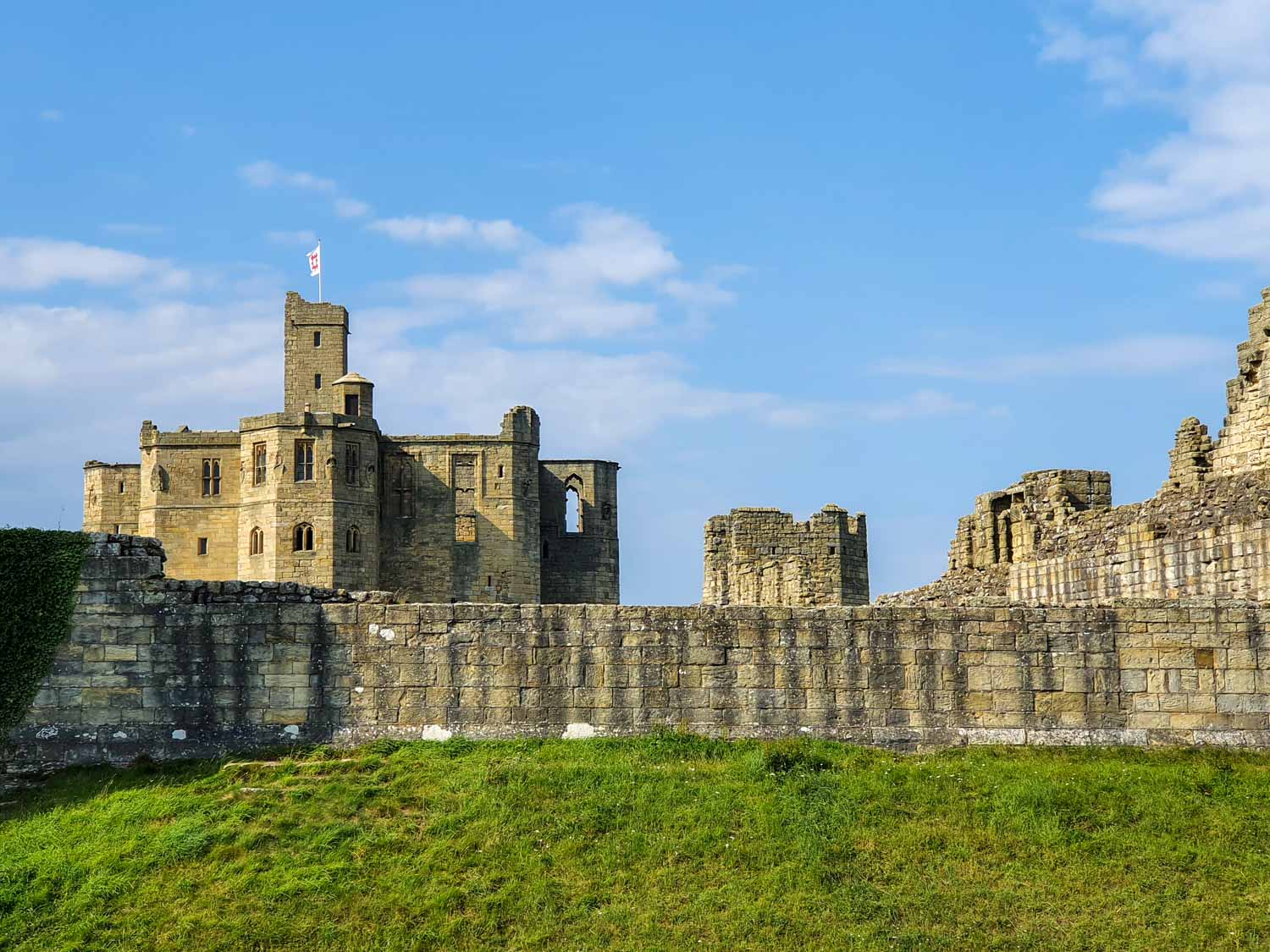 A view of Warkworth Castle Northumberland under a blue sky, with the English Heritage flag flying over the massive medieval keep - our visit to Warkworth Castle with kids