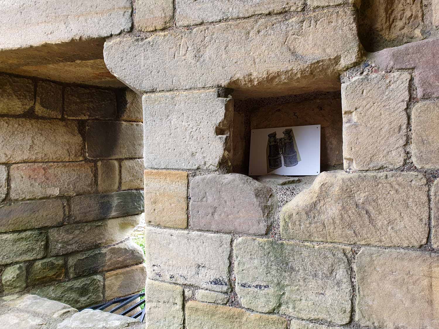 View of a clue in a stone wall on the English Heritage trail at Warkworth Castle with kids