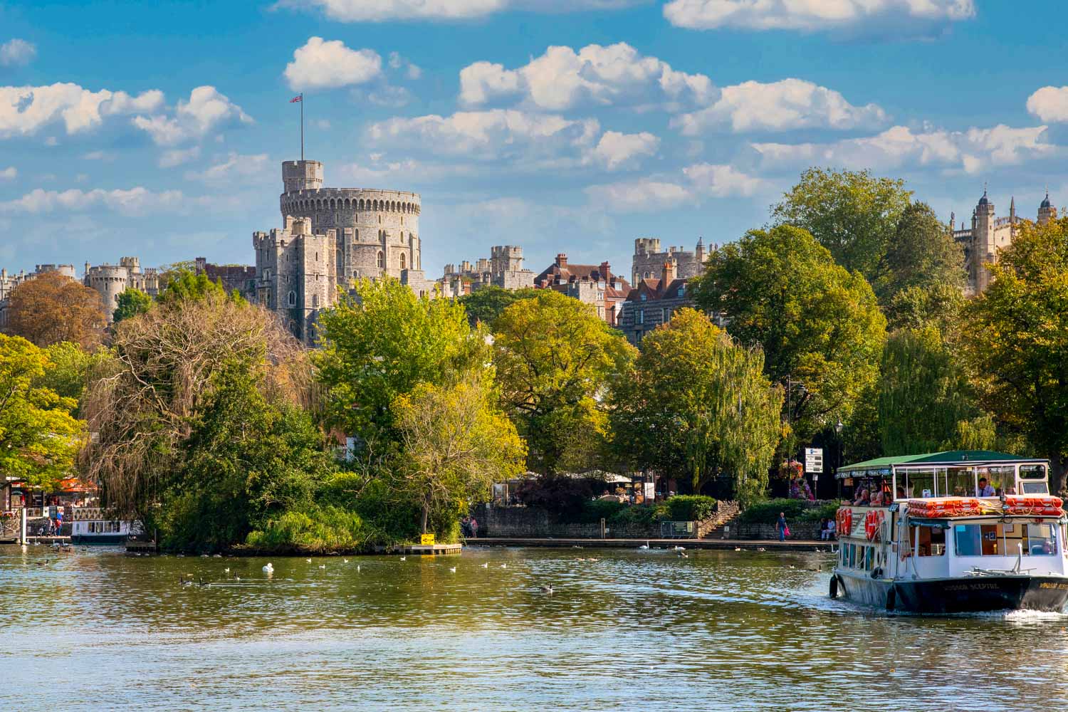 View across the river to Windsor Castle as a boat cruises along the water - my pick of the best things to do in Windsor, one of the best days out from London with kids