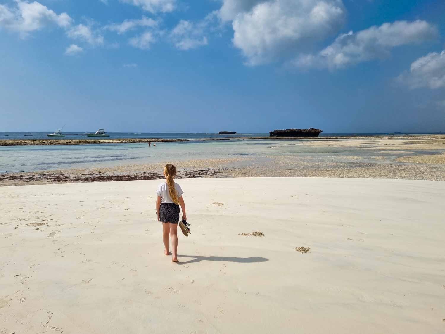 My daughter walks across the pristine white sand of Watamu beach with the turquoise sea seen in the background - my tips for visiting Kenya with kids, including planning time to relax by the coast