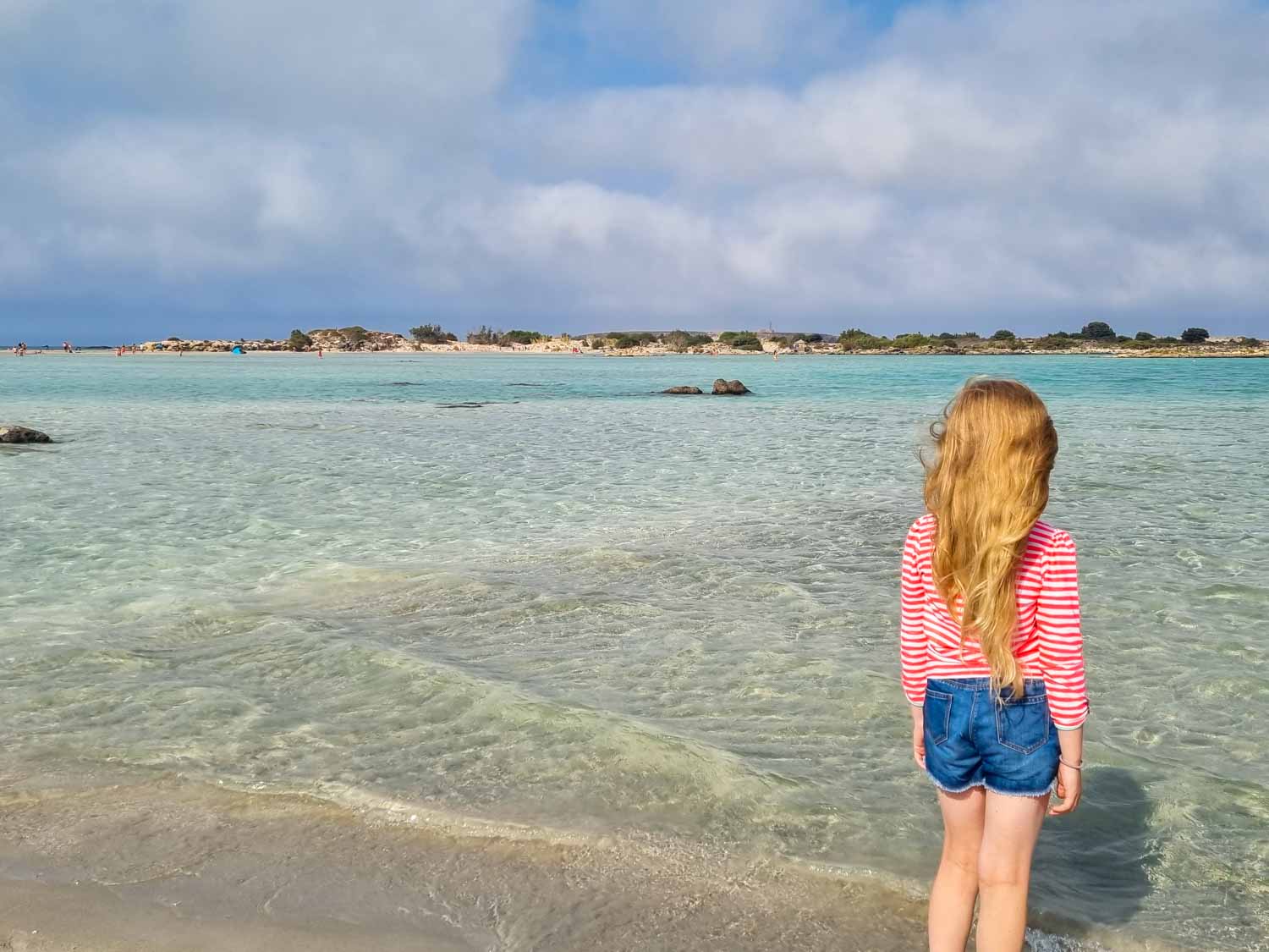 My daughter looks out at the clear turquoise water of the lagoon towards Elafonisi island in Crete my tips for visiting Elafonisi Beach with kids