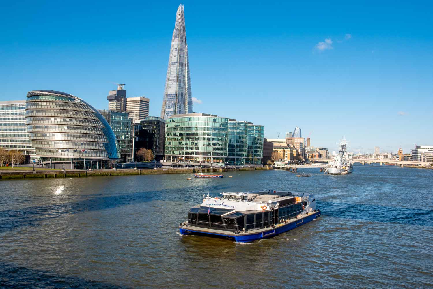 One of the City Cruises boats on the Thames in London with the Shard and HMS Belfast in the background - one of the best boat trips in London with kids